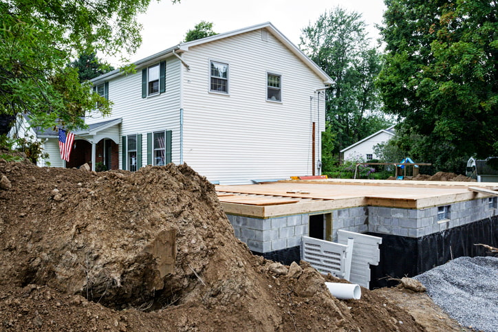 White home in green area under construction, Egress window or basement entrance being installed